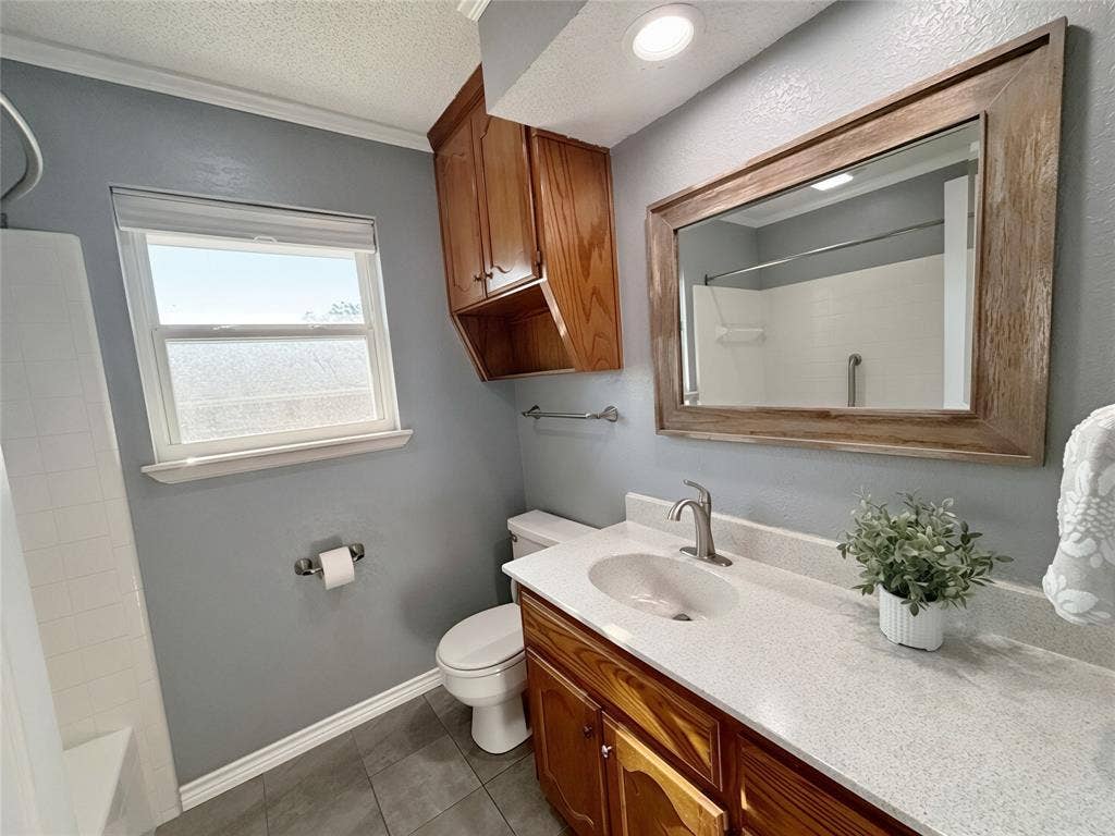 Bathroom featuring a vanity with quartz countertop, under-mount sink, integrated wood cabinetry, a framed mirror, and tile flooring