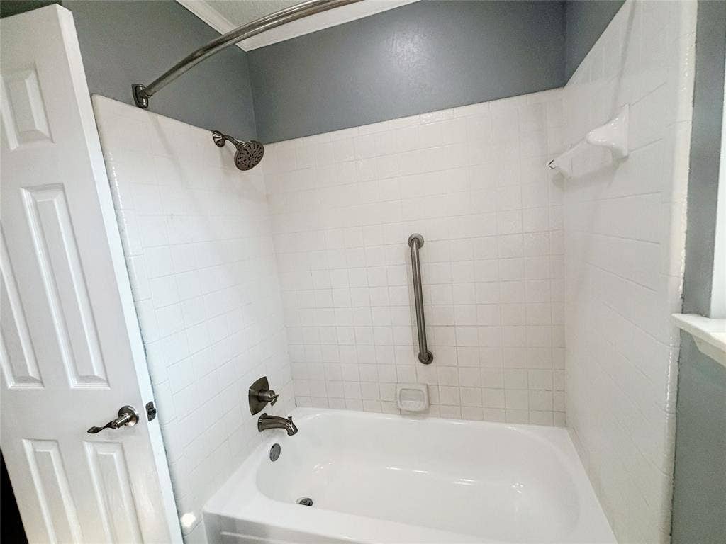 Bathtub with white subway tile surround, polished metal faucet hardware, matching shower head, integrated soap dish, and stainless steel grab bar