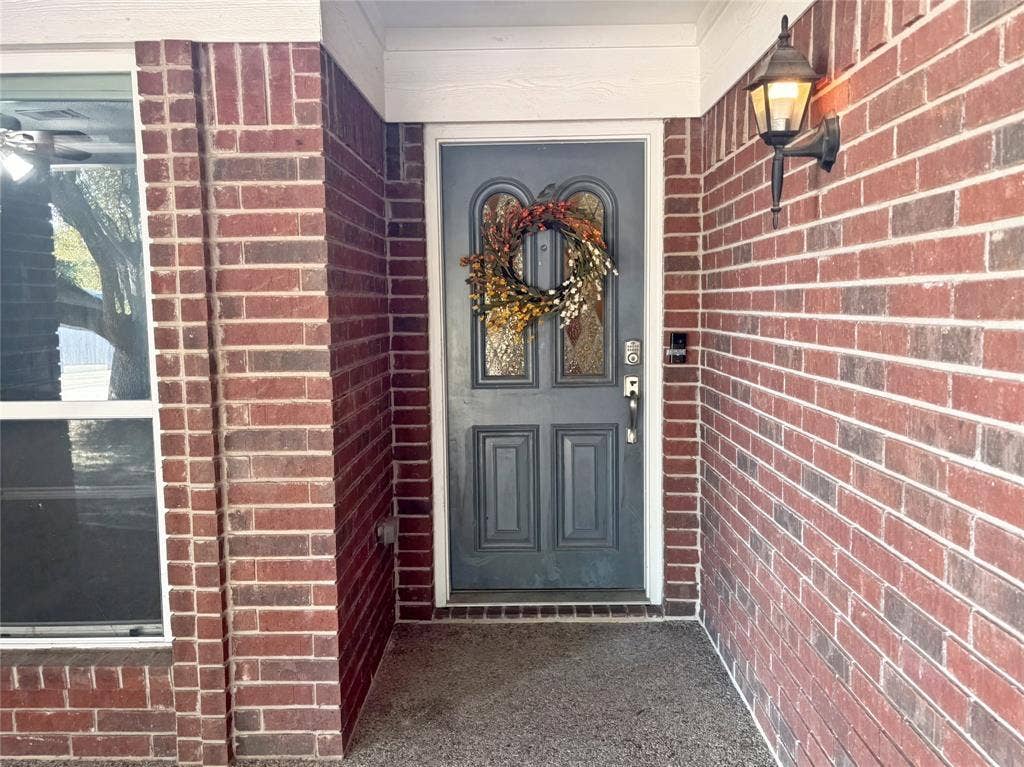 Red brick exterior featuring a covered entryway, a paneled front door with decorative glass inserts, and a wall-mounted exterior light fixture