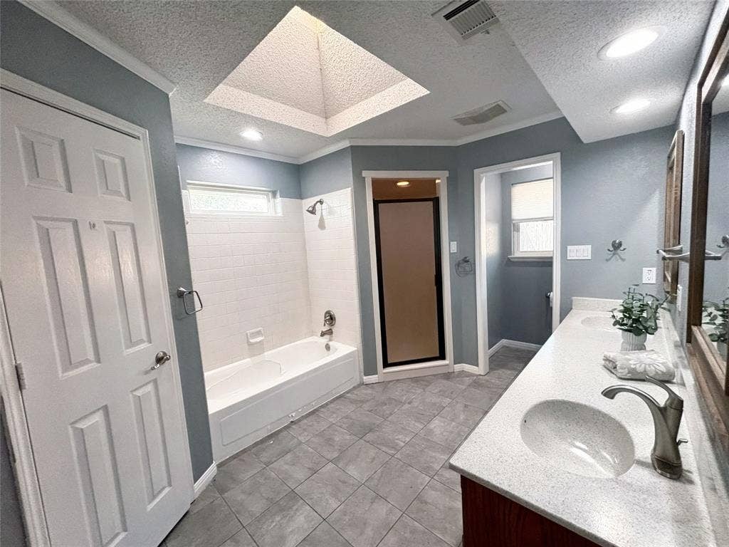 Bathroom featuring a dual-sink vanity with a solid-surface countertop, a skylight, tile flooring, and a separate bathtub and shower enclosure