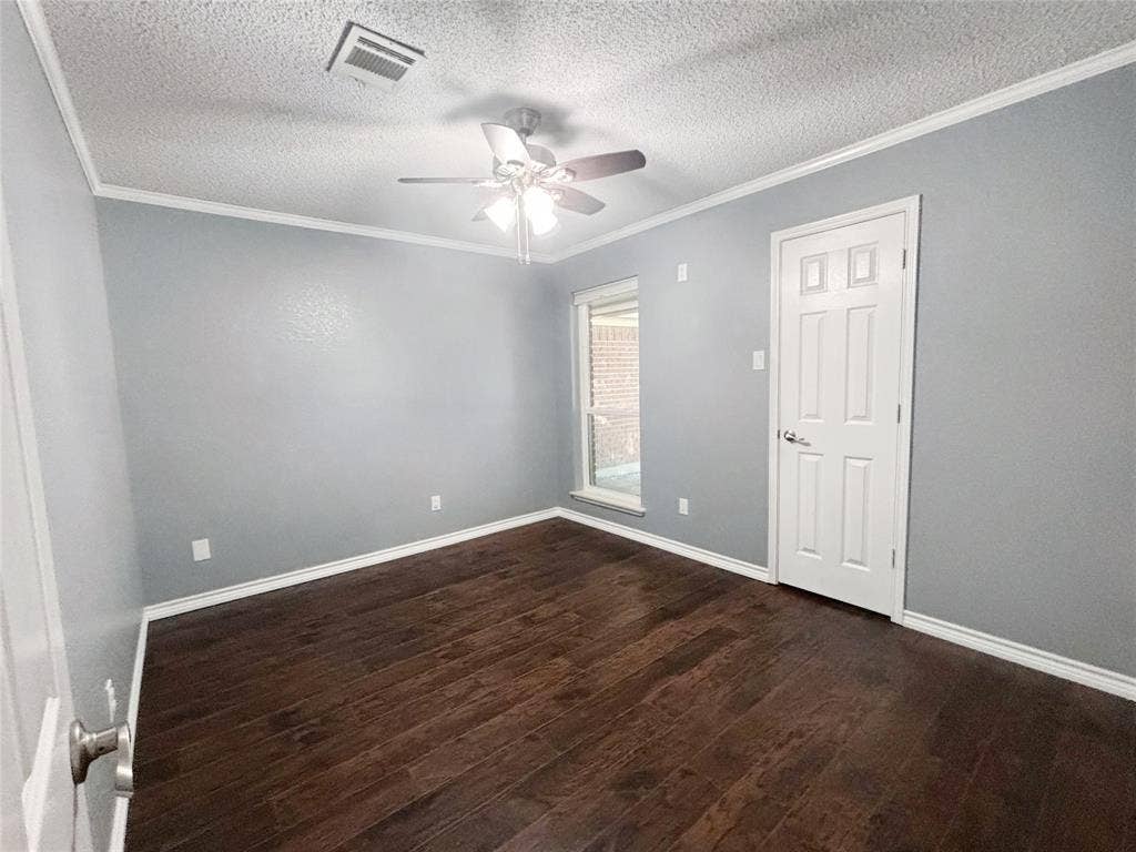Dark wood-finish flooring, neutral wall coloring, ceiling fan with integrated lighting, and a single-panel interior door