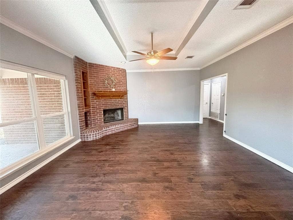 Living area featuring wood-finish flooring, a tray ceiling with a center-mounted ceiling fan, and a corner brick fireplace with a wood mantel and built-in shelving