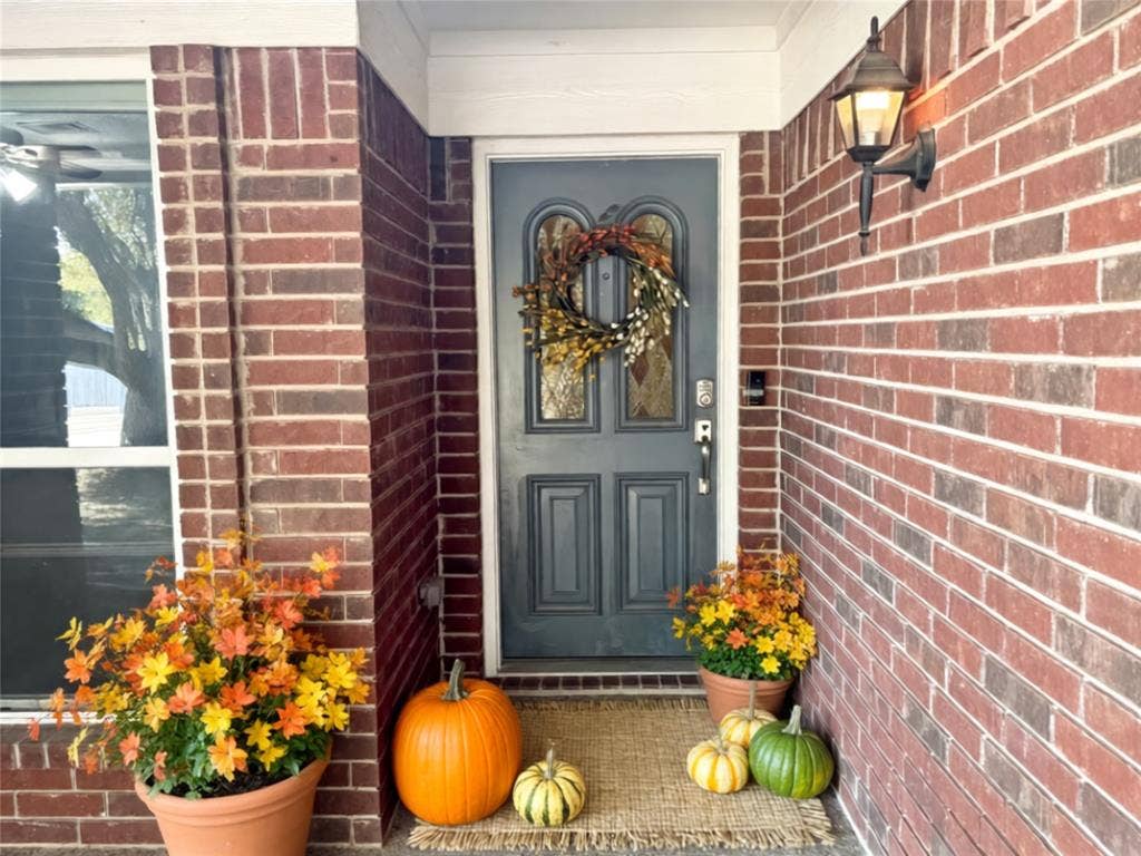 Covered entry featuring a red brick exterior, a paneled door with an arched glass insert, and a wall-mounted coach-style light fixture