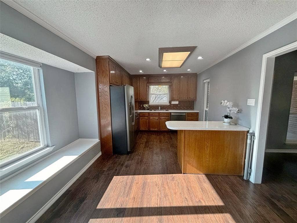 Kitchen featuring wood-finish cabinetry, a peninsula with a stone-surfaced countertop, stainless steel refrigerator, built-in recessed lighting, and a bay window with a structural window seat