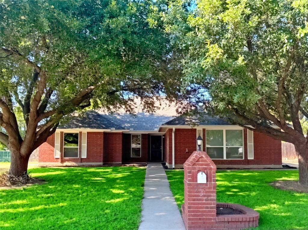 Brick exterior featuring a gabled roof, concrete walkway, matching brick mailbox with integrated planter, and mature shade trees