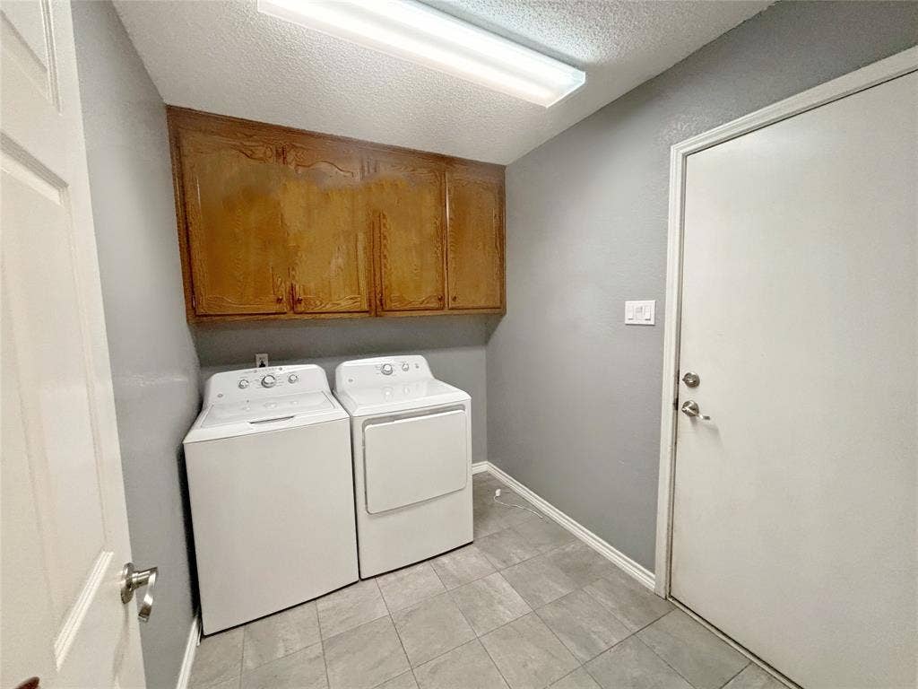 Utility area featuring tile flooring, wood-finish wall-mounted cabinetry, and a ceiling-mounted light fixture