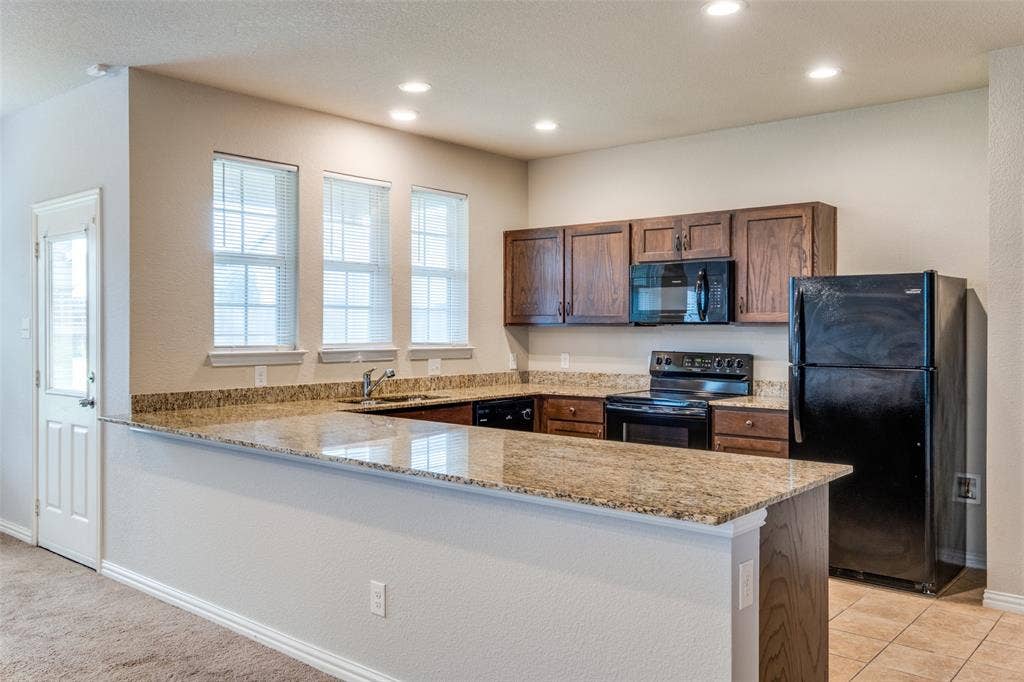4662 Ralph Lane, Dallas, TX 75227 Kitchen featuring stone countertops, an expansive breakfast bar, dark wood cabinetry, recessed lighting, and a set of three windows