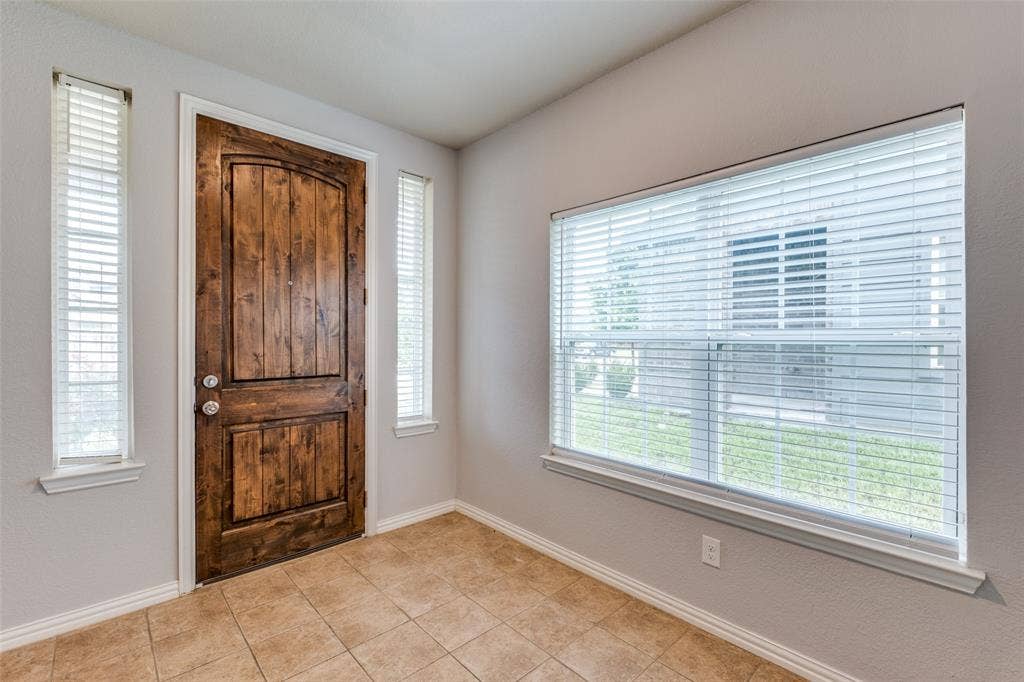 4662 Ralph Lane, Dallas, TX 75227 Entryway featuring a wood-finish arched-panel door, ceramic tile flooring, and multiple windows with horizontal blinds
