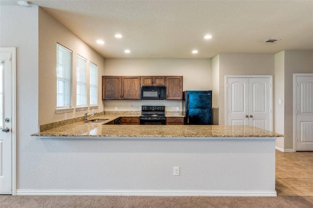 4662 Ralph Lane, Dallas, TX 75227 Kitchen featuring stone-finish countertops, dark wood cabinetry, recessed lighting, and a breakfast bar