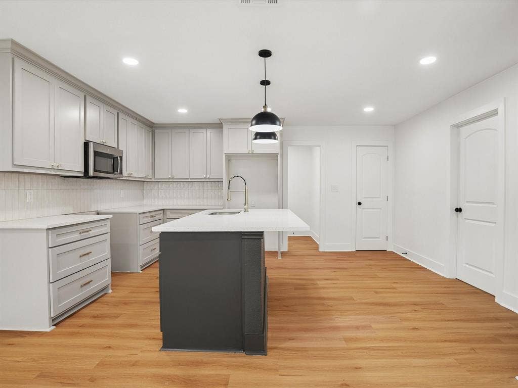 9059 Quinn Street, Dallas, TX 75217 Kitchen featuring light grey shaker-style cabinetry, quartz countertops, a contrasting dark kitchen island, recessed lighting, and wood-finish flooring