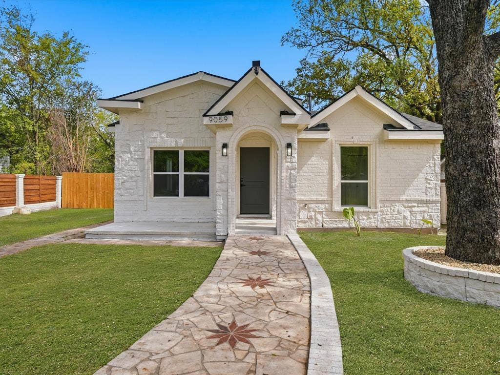 9059 Quinn Street, Dallas, TX 75217 Exterior featuring painted brick and stone facade, arched entryway, custom stone-patterned walkway, and circular stone tree planter
