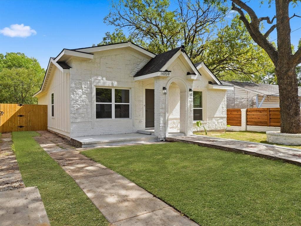 9059 Quinn Street, Dallas, TX 75217 Exterior façade featuring white stone and vertical siding, covered entryway with arched portico, and wood-finish perimeter fencing