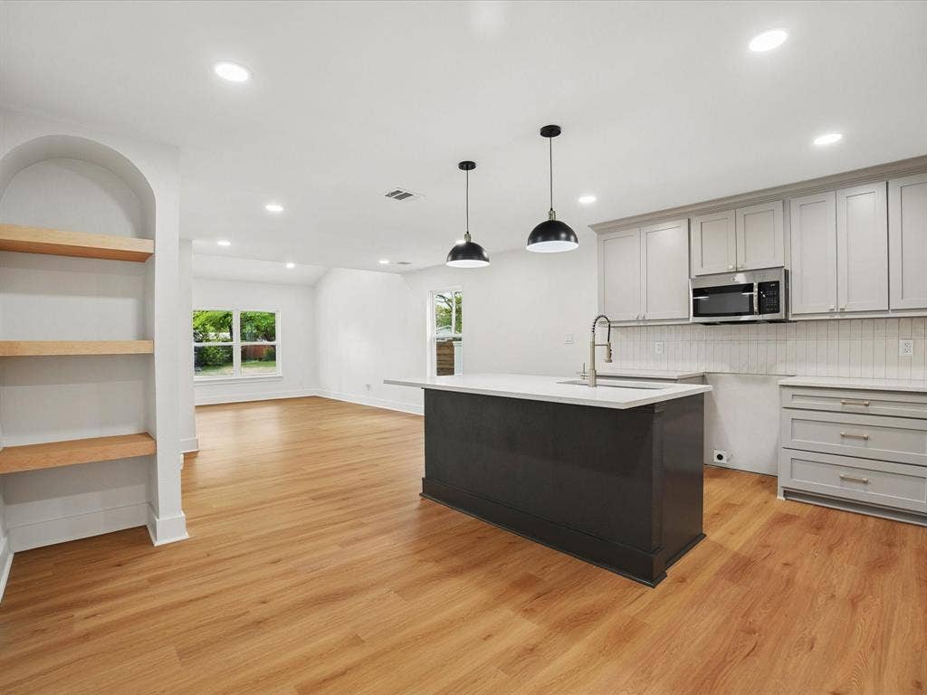 9059 Quinn Street, Dallas, TX 75217 Kitchen featuring a dark-toned center island with light stone countertop, recessed lighting, wood-finish flooring, built-in recessed shelving, and a combination of grey cabinetry and stainless steel microwave
