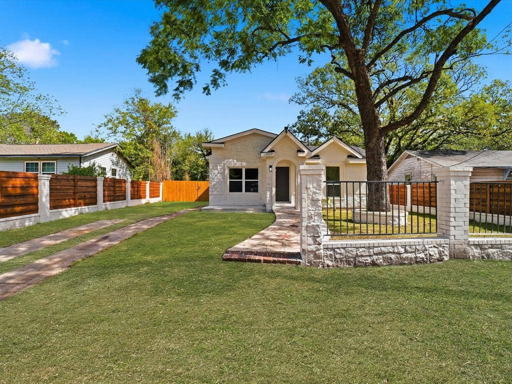 9059 Quinn Street, Dallas, TX 75217 Light-colored masonry exterior with a gabled roofline, stone perimeter fencing, wrought iron gated entrance, and a paved walkway leading to the front entry