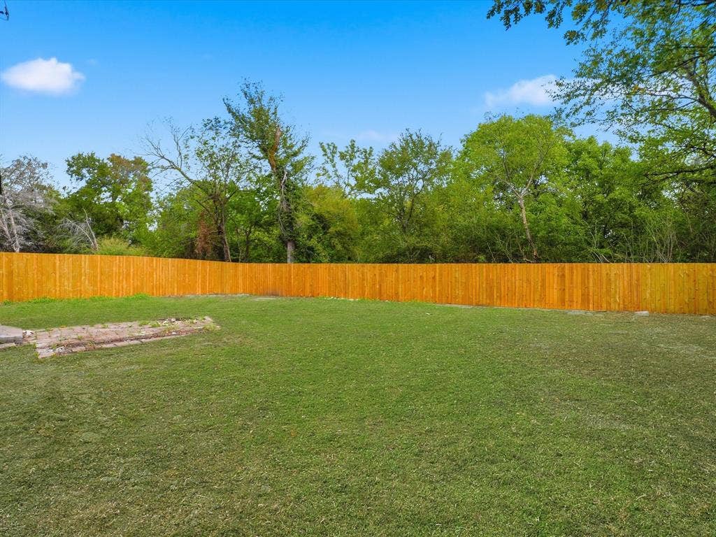 9059 Quinn Street, Dallas, TX 75217 Expansive backyard featuring a large grass lawn, a wood-panel privacy fence, and mature trees