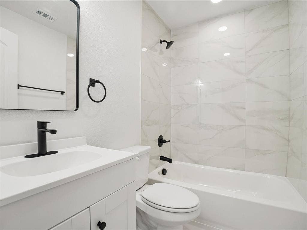 9059 Quinn Street, Dallas, TX 75217 Bathroom featuring a white vanity with a solid surface countertop, matte black faucet, rectangular mirror with a black frame, and a tub-shower combination with floor-to-ceiling neutral-toned tile surround