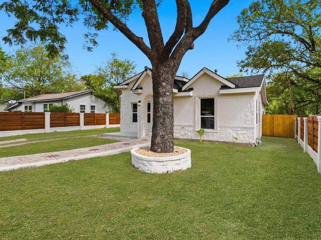 9059 Quinn Street, Dallas, TX 75217 Painted brick exterior featuring a multi-gabled roofline, stone-finished masonry, wood-and-masonry perimeter fencing, and a stone-paver walkway