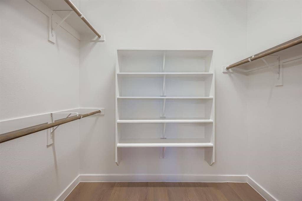 1204 Pebblebrook Drive, McKinney, TX 75071 Storage area featuring custom white built-in shelving, wood-finish hanging rods, and wood-finish flooring