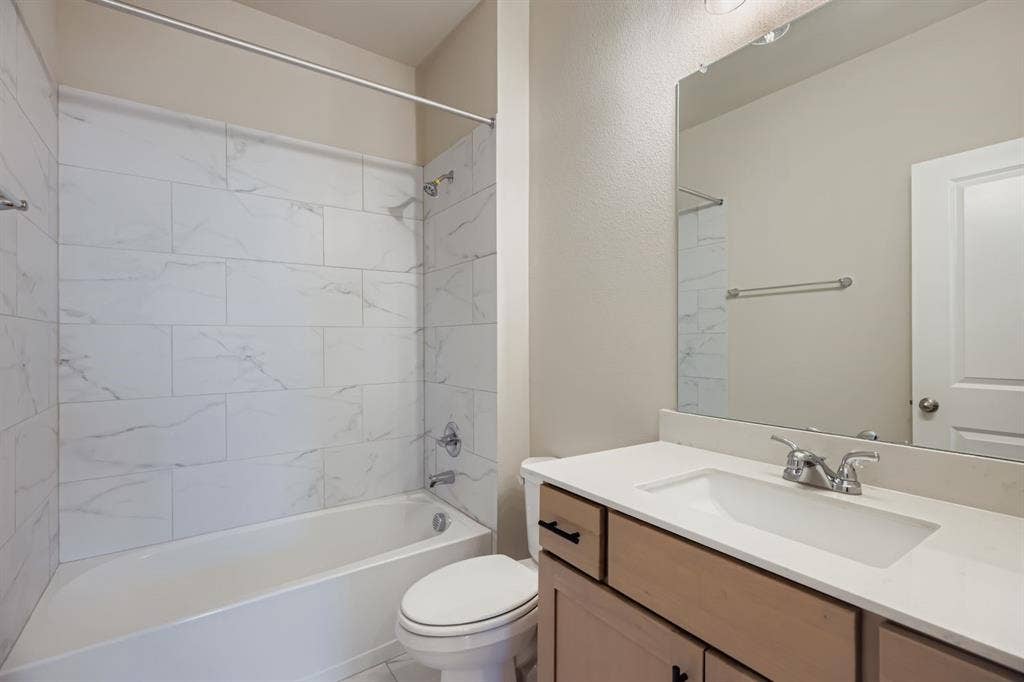 1204 Pebblebrook Drive, McKinney, TX 75071 Bathroom featuring a vanity with a light-toned wood finish, white countertop, integrated sink, and chrome fixtures, paired with a shower-tub combo enclosed by white tile with a stone-pattern finish and a full-width vanity mirror