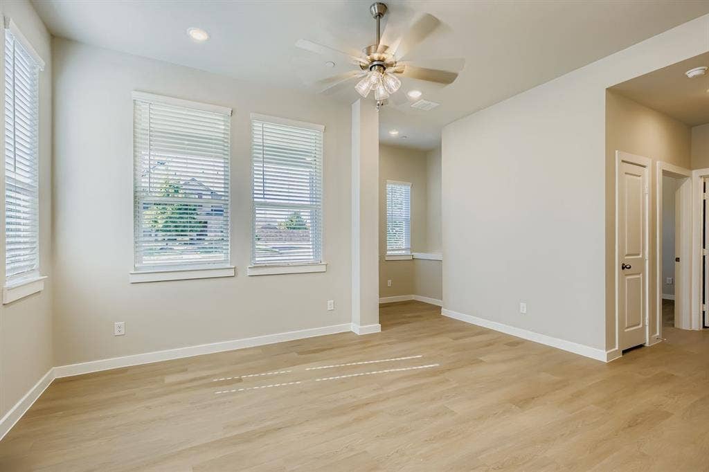 1204 Pebblebrook Drive, McKinney, TX 75071 Neutral-toned interior space featuring wood-finish flooring, recessed lighting, a brushed-metal ceiling fan with integrated glass lighting, and multiple windows with installed blinds