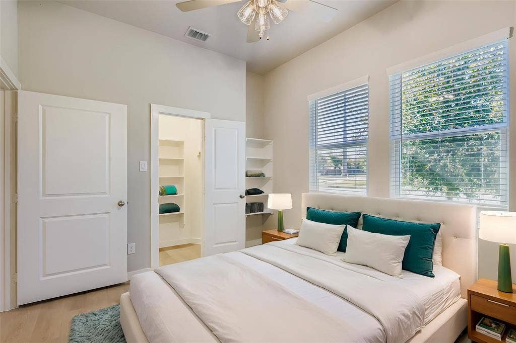 1204 Pebblebrook Drive, McKinney, TX 75071 High-ceilinged room featuring wood-finish flooring, dual windows with blinds, a ceiling fan with light fixture, and built-in wall shelving