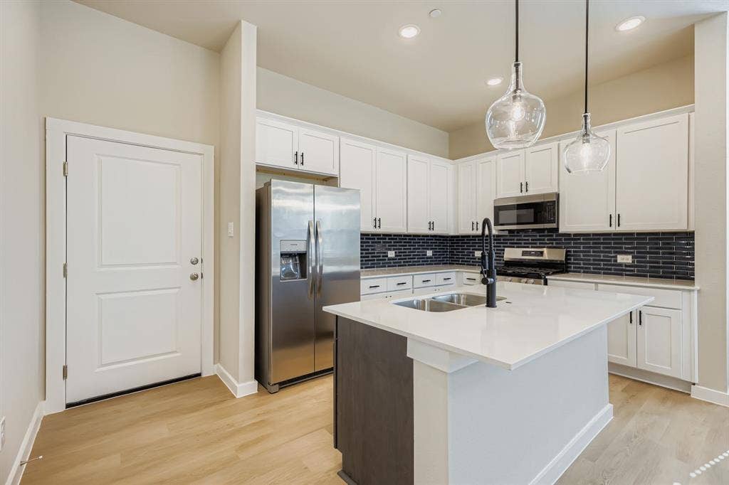 1204 Pebblebrook Drive, McKinney, TX 75071 Kitchen featuring white cabinetry, a center island with a stone-finish countertop, dark subway tile backsplash, stainless steel appliances, and pendant lighting