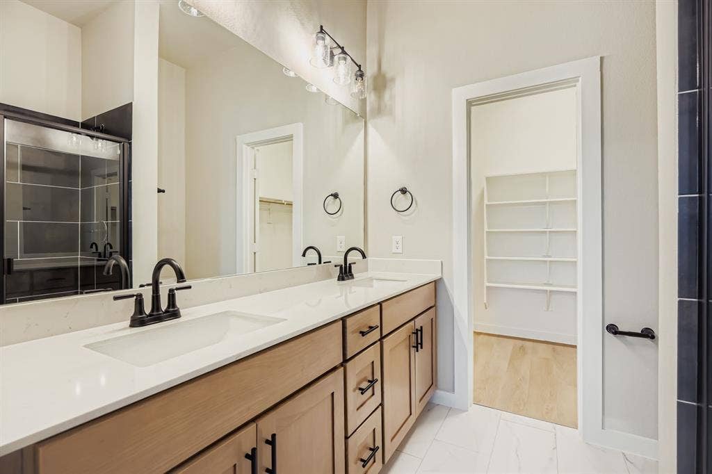 1204 Pebblebrook Drive, McKinney, TX 75071 Dual-sink vanity with light-tone wood cabinetry, quartz countertops, matte black fixtures, and a wall-to-wall mirror