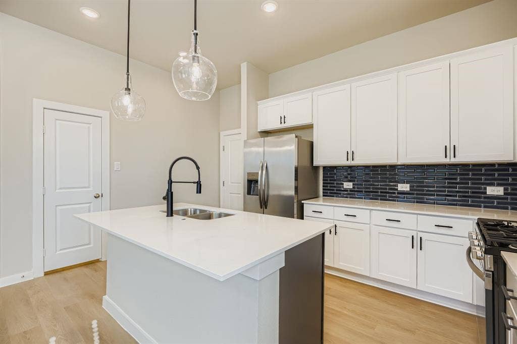 1204 Pebblebrook Drive, McKinney, TX 75071 Kitchen featuring white shaker-style cabinetry, quartz countertops, a dark-toned subway tile backsplash, a central island with a double-basin sink and matte black faucet, and pendant lighting