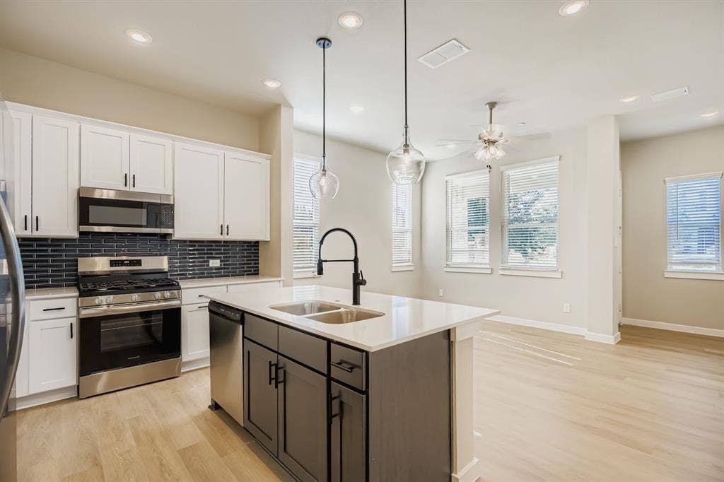1204 Pebblebrook Drive, McKinney, TX 75071 Kitchen featuring white cabinetry, a contrasting dark-toned kitchen island, stone-surface countertops, a dark-toned tile backsplash, and stainless-steel appliances