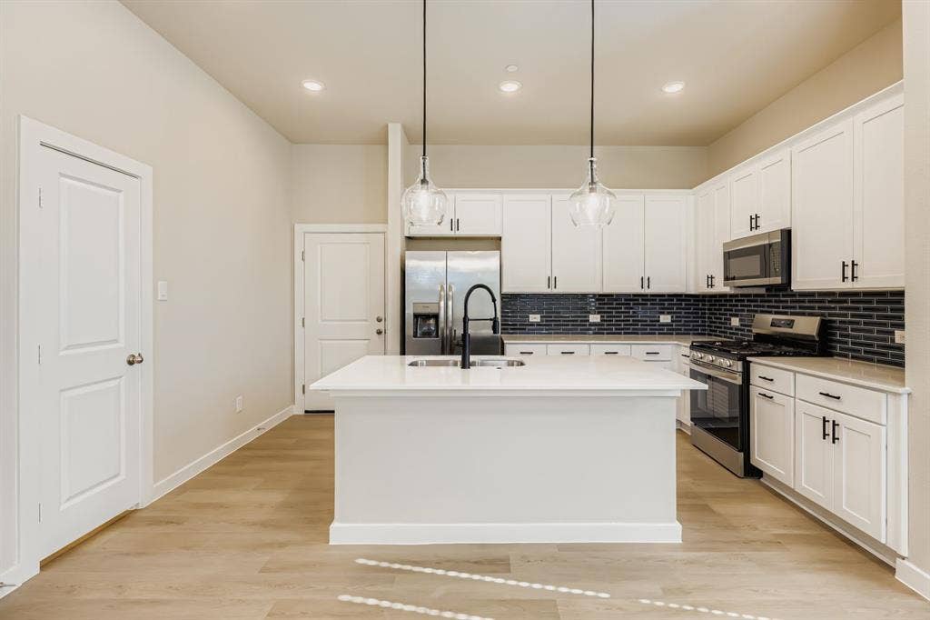 1204 Pebblebrook Drive, McKinney, TX 75071 Kitchen featuring white cabinetry, quartz countertops, a central island with a high-arch faucet, dark subway tile backsplash, and wood-finish flooring