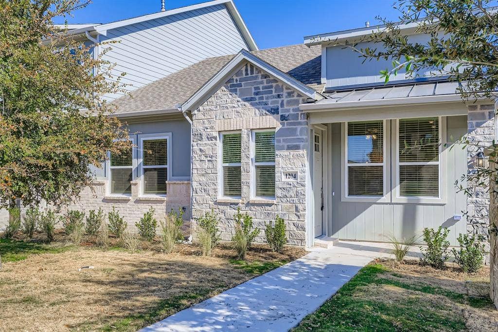 1204 Pebblebrook Drive, McKinney, TX 75071 Exterior featuring stone veneer masonry, vertical panel siding, a metal roof accent over the entryway, and multi-pane windows