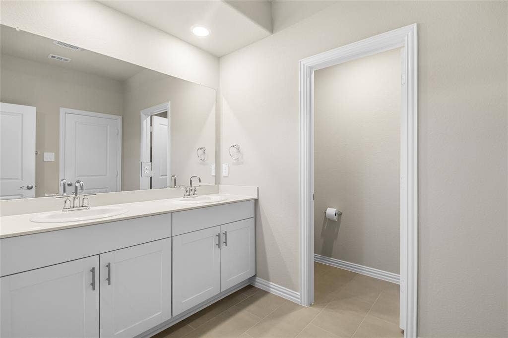 614 Martell Road, Lowry Crossing, TX 75069 Dual-sink vanity featuring white cabinetry, solid-surface countertop, chrome fixtures, and a wall-to-wall mirror with recessed ceiling lighting