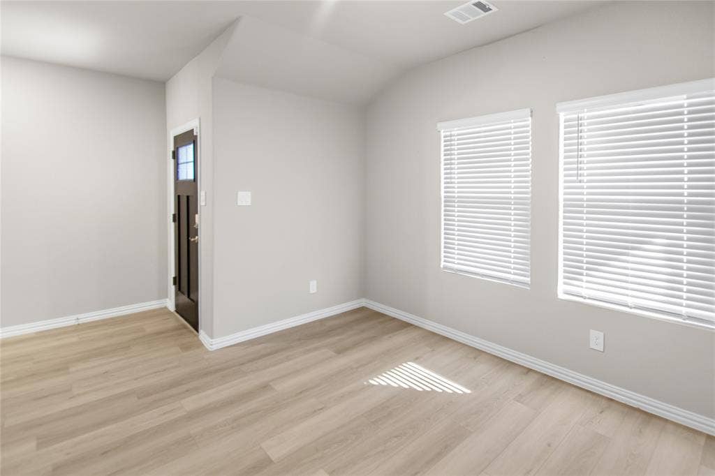 614 Martell Road, Lowry Crossing, TX 75069 Interior room featuring wood-finish flooring, neutral wall paint, two windows with white horizontal blinds, and a dark-toned exterior door with an inset glass panel