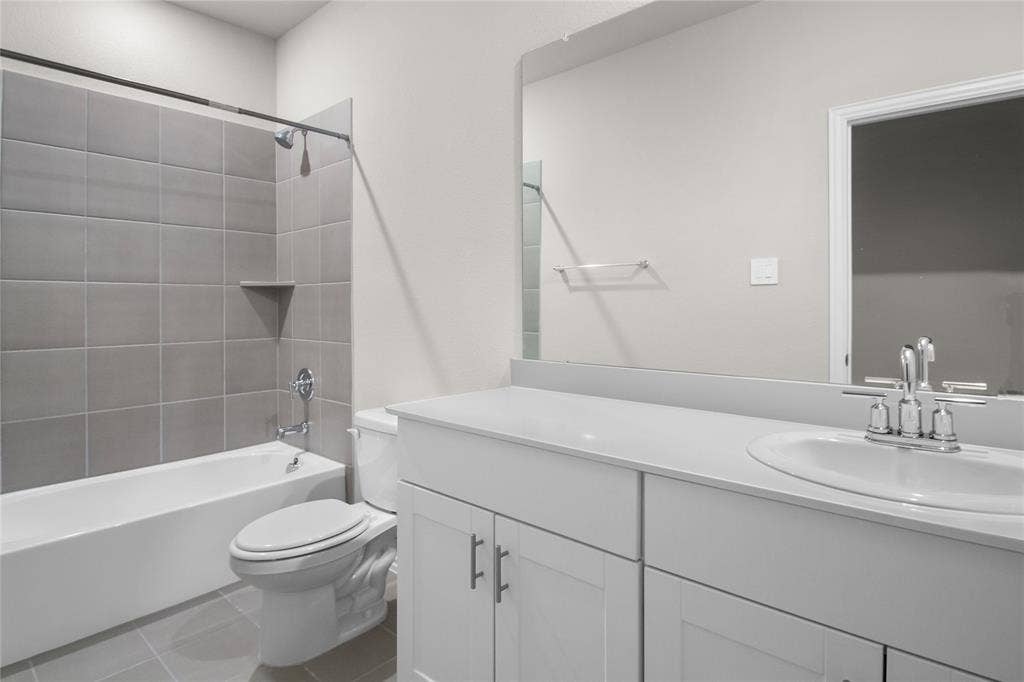 614 Martell Road, Lowry Crossing, TX 75069 Bathroom featuring a white vanity with a composite countertop, an integrated sink, a large wall-mounted mirror, and a tub-shower combination with oversized grey ceramic tile surround