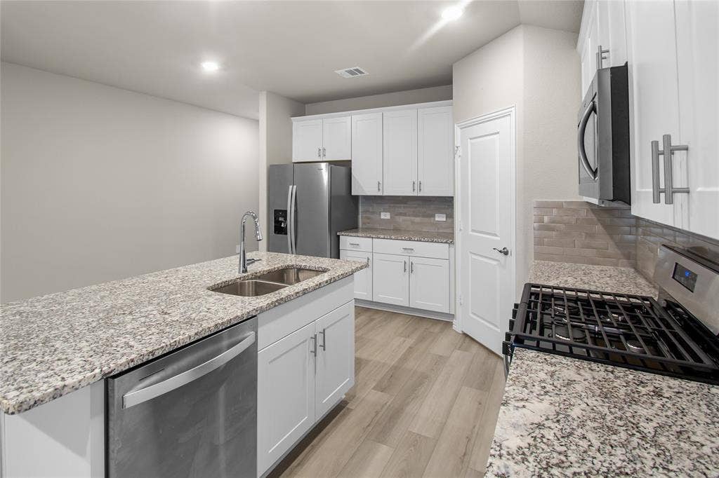 614 Martell Road, Lowry Crossing, TX 75069 Kitchen featuring white shaker-style cabinetry, stone-finish countertops, subway tile backsplash, stainless steel appliances, and wood-finish flooring