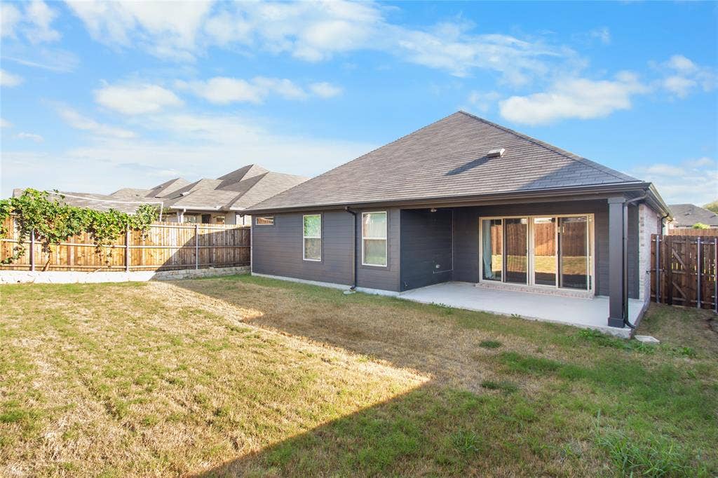 614 Martell Road, Lowry Crossing, TX 75069 Rear exterior featuring dark-toned siding, a covered concrete patio, sliding glass door access, and a fenced yard with wood perimeter fencing