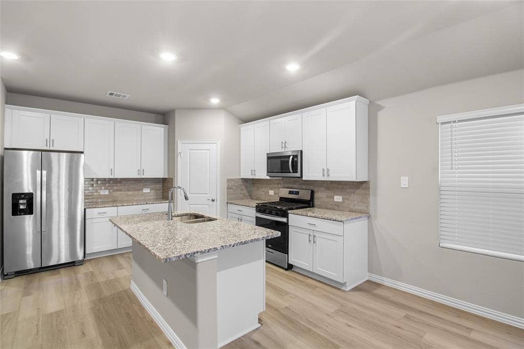 614 Martell Road, Lowry Crossing, TX 75069 Kitchen featuring white shaker-style cabinetry, stone-surface countertops, wood-finish flooring, a central island with an undermount sink, and stainless steel appliances