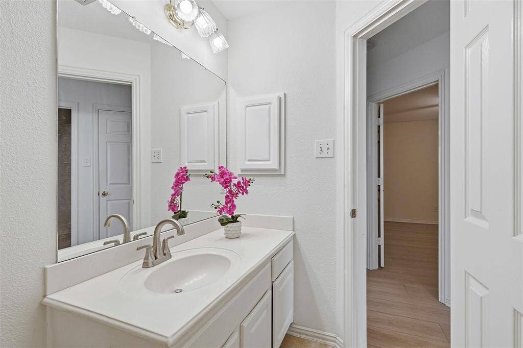 2902 Glen Hollow Court, McKinney, TX 75072 Bathroom vanity featuring a solid-surface countertop, an integrated oval sink with a brushed-nickel faucet, extensive wall-to-wall mirror, and multi-bulb overhead lighting fixture