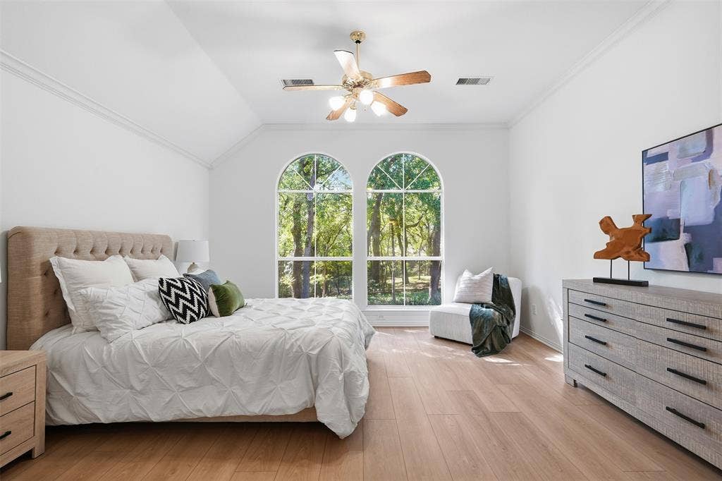 2902 Glen Hollow Court, McKinney, TX 75072 Primary bedroom featuring wood-finish flooring, vaulted ceilings, dual arched windows, and a multi-blade ceiling fan with integrated lighting