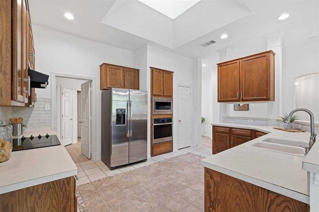 2902 Glen Hollow Court, McKinney, TX 75072 Kitchen featuring custom wood cabinetry, stainless steel appliances including a built-in oven and microwave, recessed lighting, a large ceiling skylight, and solid-surface countertops