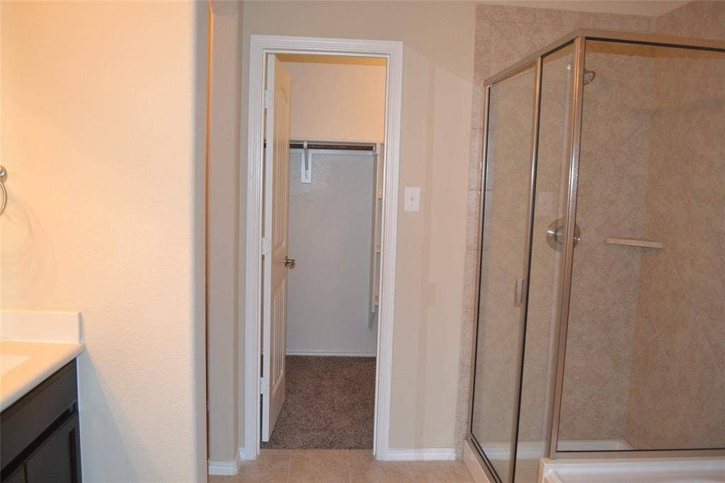 Bathroom featuring a glass-enclosed shower with tile surround, dark-finish vanity cabinetry, and a walk-in closet with built-in shelving