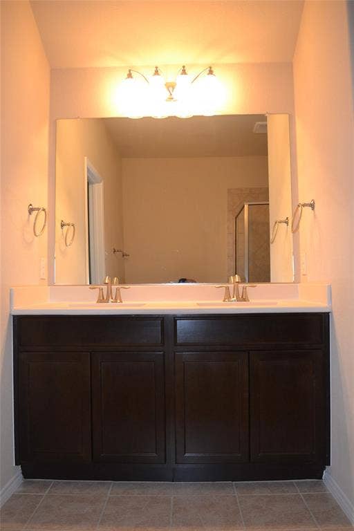 Dual-sink vanity featuring dark wood-finish cabinetry, solid surface countertop, metallic finish faucets, and a large-format vanity mirror with integrated light fixture