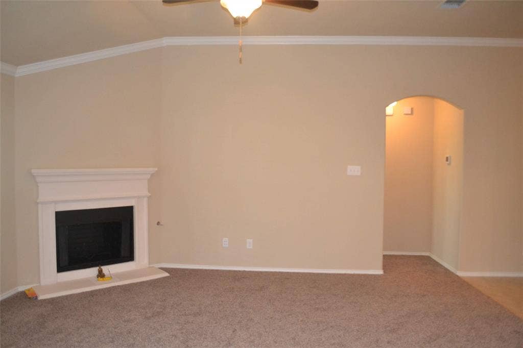 Vaulted ceiling with a central ceiling fan, fireplace featuring a white mantle and surround, and an arched entryway