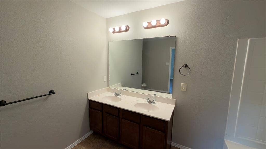 8808 Irish Bend Drive, Fort Worth, TX 76123 Double-vanity cabinet with a white countertop, dual integrated sinks, wall-to-wall mirror, and dark-finish hardware