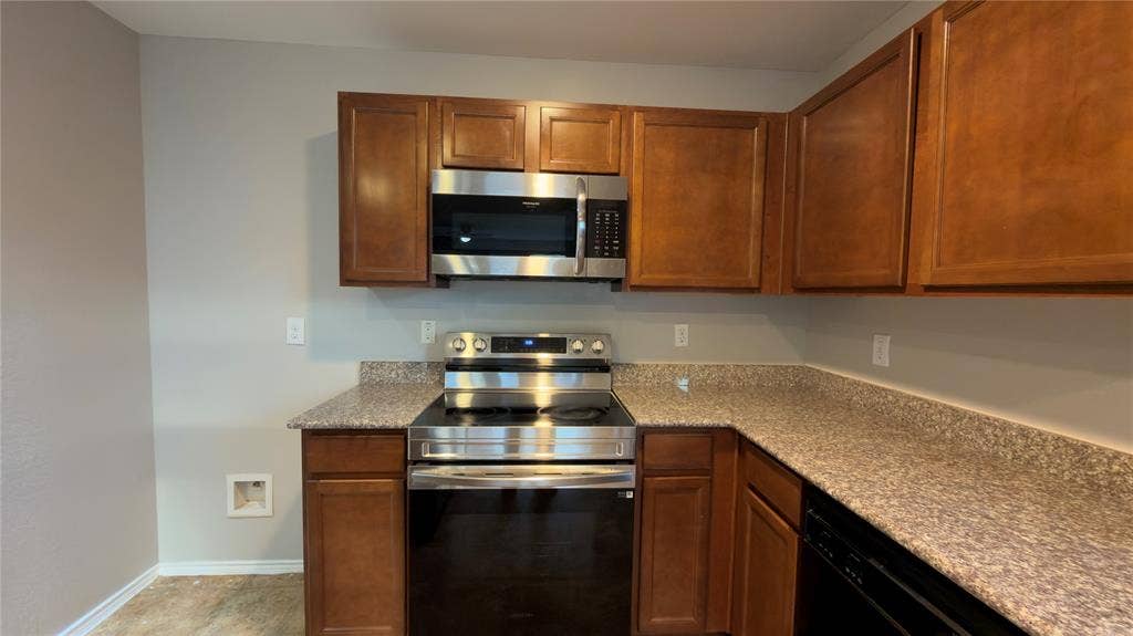 8808 Irish Bend Drive, Fort Worth, TX 76123 Kitchen featuring stained wood cabinetry, stone-finish countertops, and stainless steel appliances including a built-in microwave and range