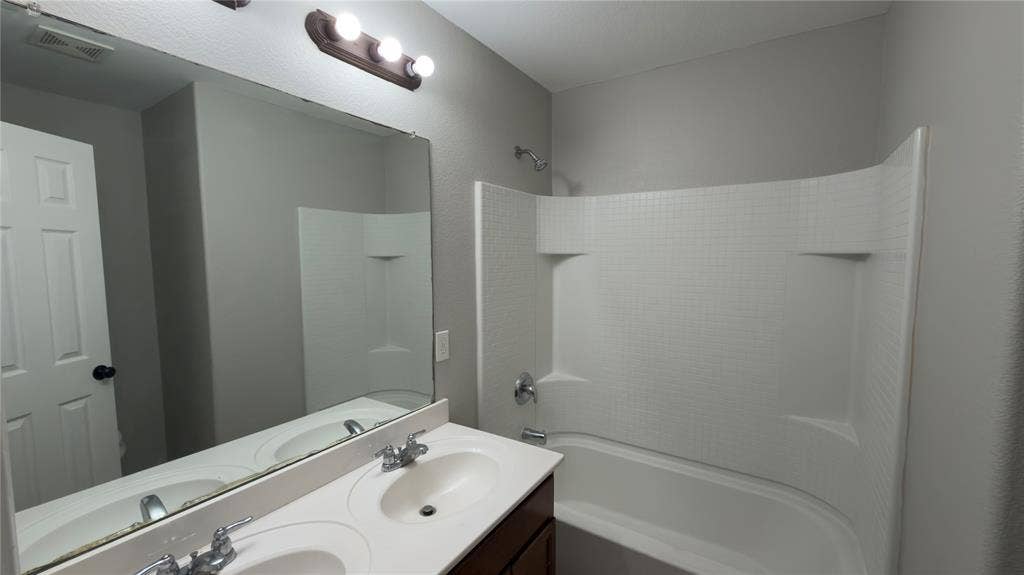 8808 Irish Bend Drive, Fort Worth, TX 76123 Double-sink vanity with a solid-surface countertop, full-width vanity mirror, triple-bulb light fixture, and a tub-shower combination featuring a molded surround