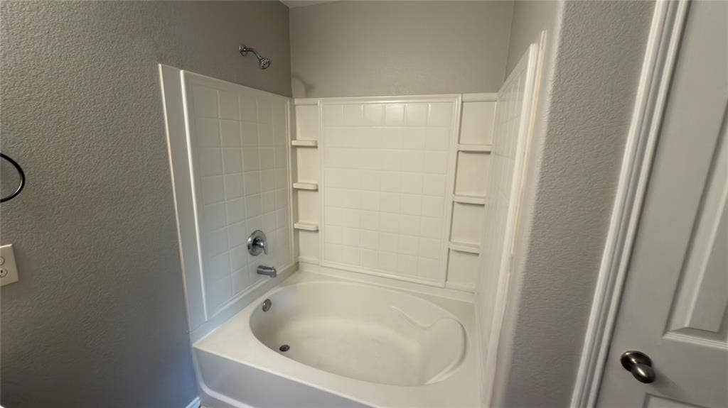 8808 Irish Bend Drive, Fort Worth, TX 76123 Built-in deep soaking tub with integrated shower head, tiled wall surround, and multiple recessed storage niches