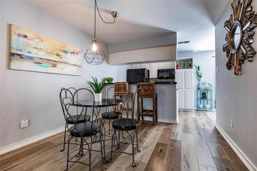 Wood-finish flooring, geometric metal pendant lighting, breakfast bar, and white cabinetry