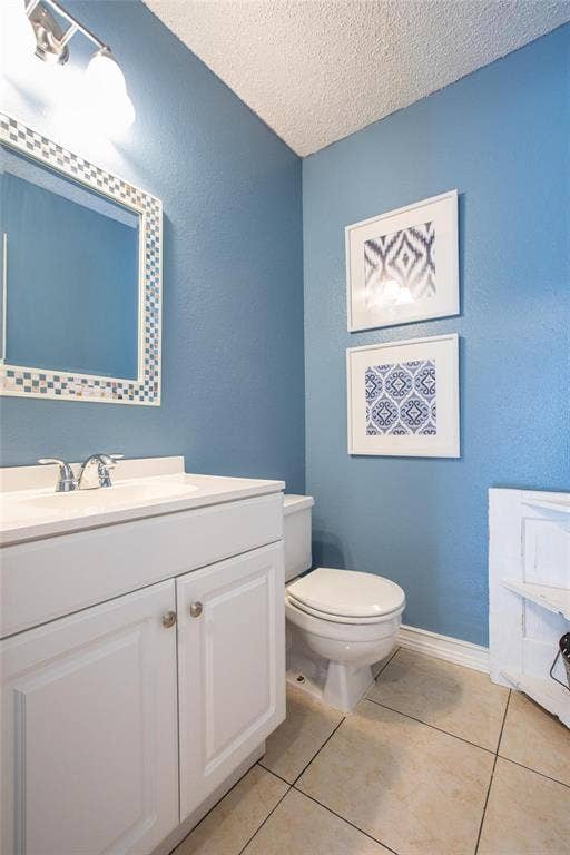 White vanity cabinet with an integrated sink, chrome dual-handle faucet, square-tiled flooring, and a decorative framed mirror