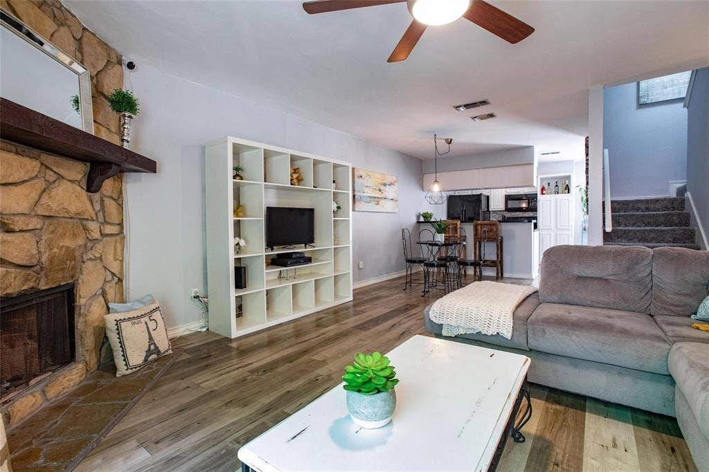 Floor-to-ceiling natural stone fireplace with a thick timber mantel, wood-finish flooring, built-in shelving unit, and a ceiling fan with integrated lighting